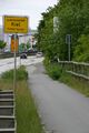 Konrad-Adenauer-Damm an der Stadtgrenze. Rechts bei der teilweise verdeckten Normaluhr schiebt jemand sein Fahrrad auf den Weg Nach Schwarzland.