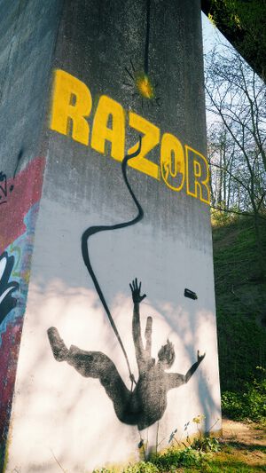 Graffito an einem der Pfeiler der Olympiabrücke. Es zeigt einen Sprayer, der von dem Pfeiler abstürzt, weil sein Halteseil gerissen ist. Mit gelber Farbe hatte er den Schriftzug „RAZOR“ gesprayt und nicht fertiggstellt.